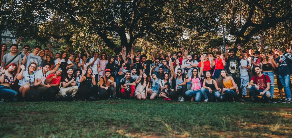 A diverse group of people gathering outdoors in a park, celebrating together with raised hands.