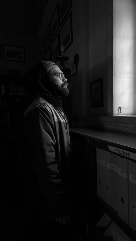 Moody black and white portrait of a man gazing through a window, capturing introspection.